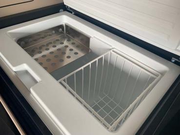 Mercedes Marco Polo Kühlschrank mit installiertem glänzenden Edelstahlregal, gefüllt mit Lebensmitteln und Getränken.